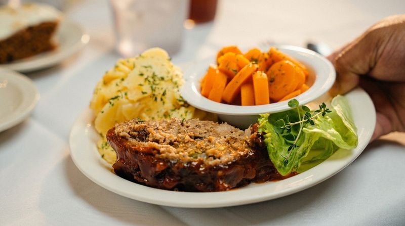 A plated meal of meatloaf, mashed potatoes, glazed carrots and fresh greens